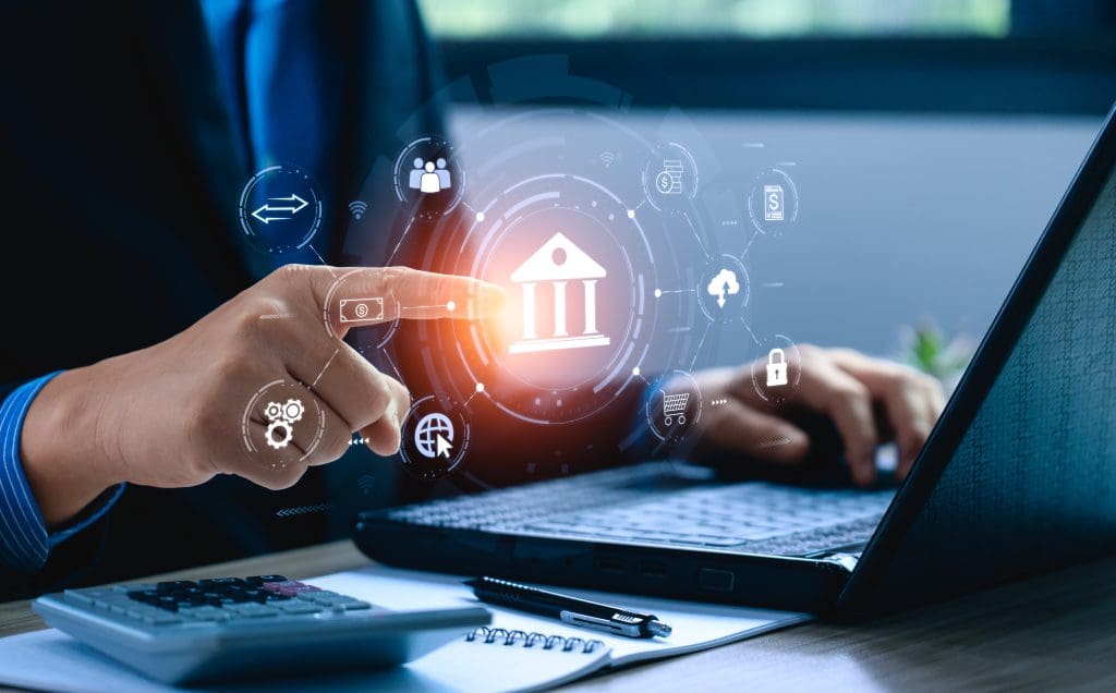 A person using a laptop touches an icon of a bank hovering above the computer.