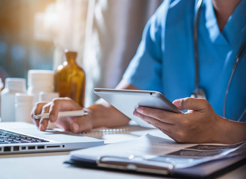 A medical professional uses a laptop and a cell phone.